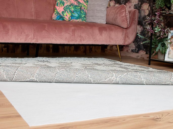 Sous-couche blanche glissée sous un tissage clair, devant un canapé rose