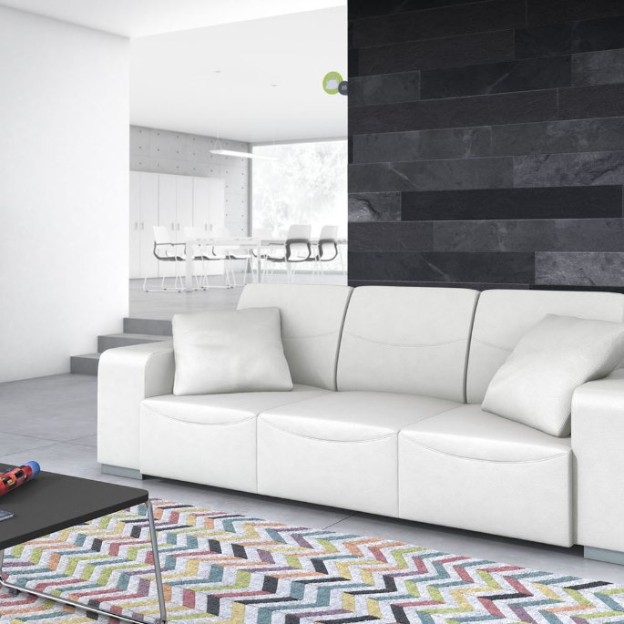 Espace de repos avec un large sofa clair, mur sombre et tapis coloré, dans une pièce lumineuse
