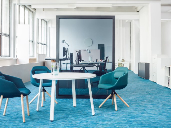 Espace de discussion sur moquette bleue avec sièges enveloppants bleu canard autour d'une table ronde