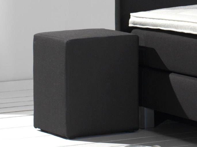 Cube de rangement bas posé au ras du sol contre un lit tapissier de grande hauteur