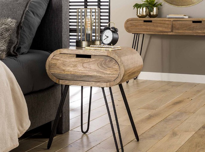 Meuble de nuit rond en bois posé sur trois pieds fins près d'un lit