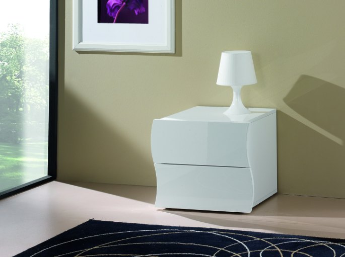 Meuble de nuit laqué surmonté d’une lampe, contre un mur vert olive