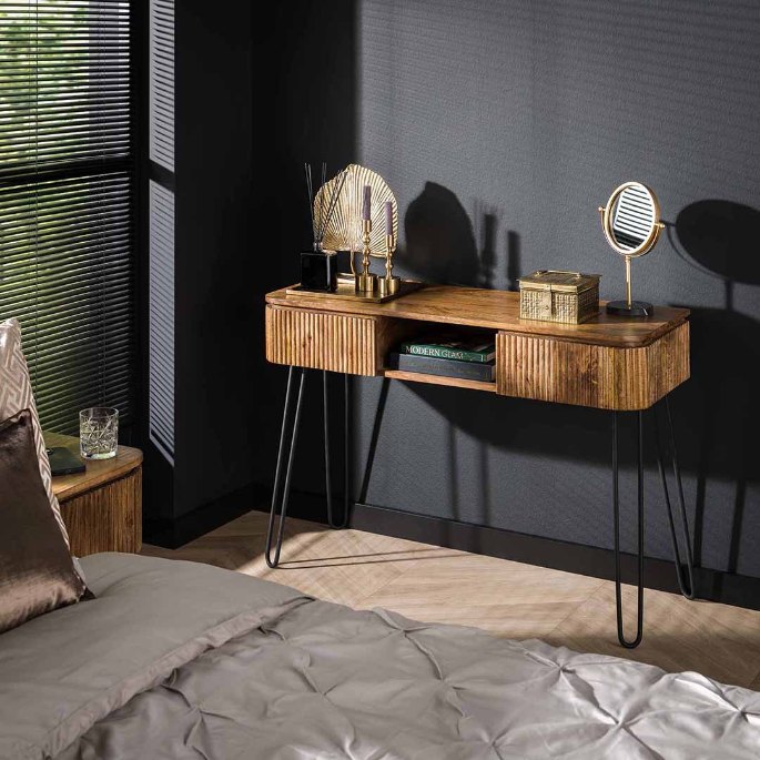 Petit meuble en manguier sur pieds épingle, lampe dorée et miroir de table contre un mur sombre