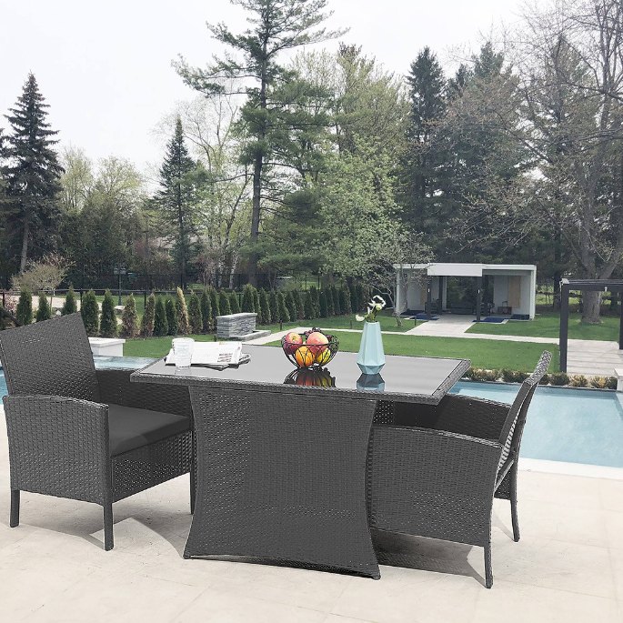 Plateau en verre entouré de fauteuils en fibres tressées sombres au bord d’une piscine