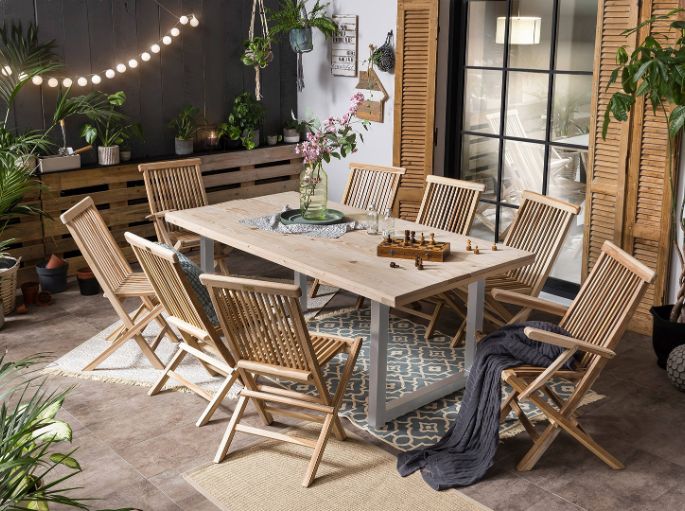 Coin de plein air éclairé par des guirlandes, meublé de sièges pliants et d’une grande table