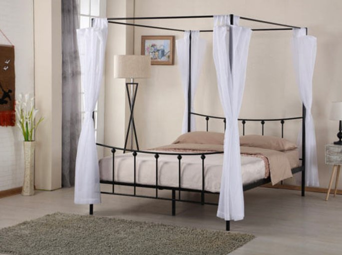 Ciel de lit à quatre colonnes en fer sombre et voiles clairs dans une chambre beige