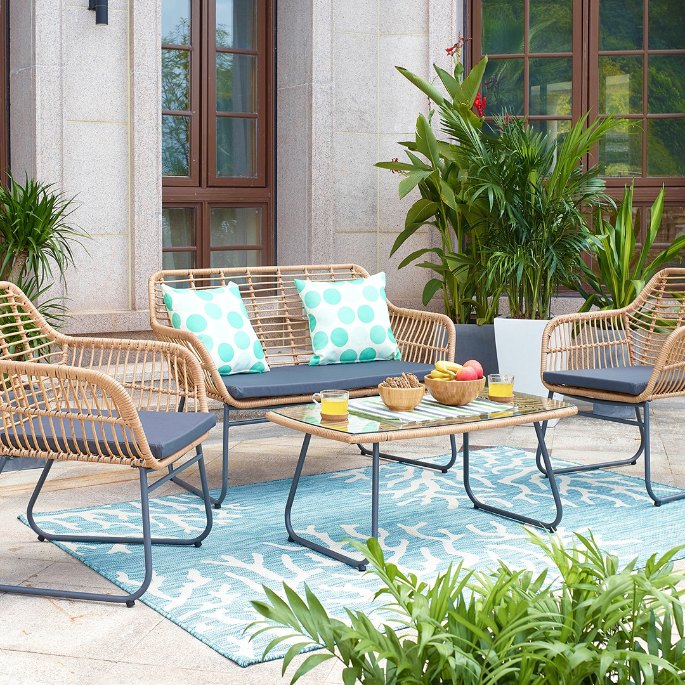 Mobilier d’extérieur en fibres tressées ton miel avec coussins clairs sur une terrasse