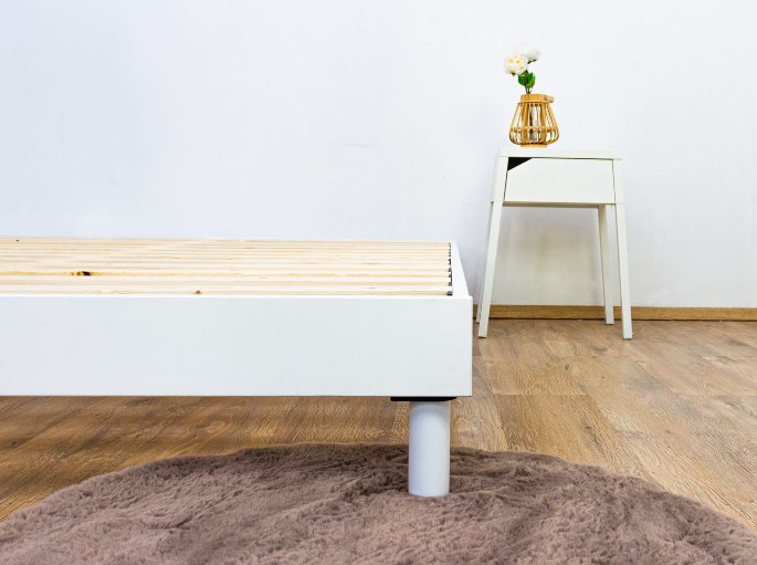 Piètement cylindrique clair fixé sous une ossature en bois de support de couchage