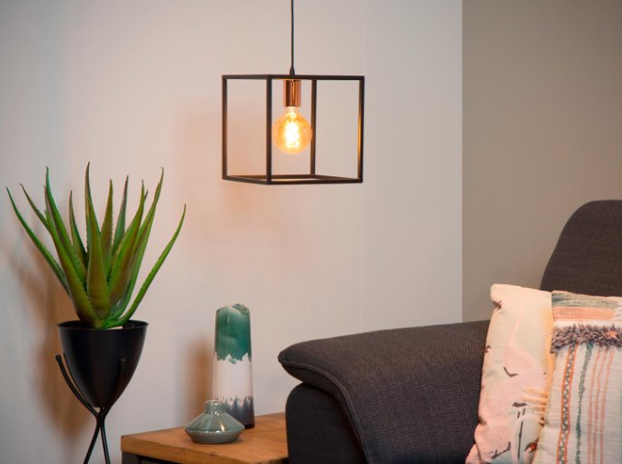Cage métallique à ampoule filament au-dessus d'un fauteuil gris et d'une plante