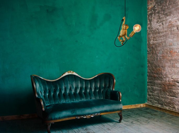Petit luminaire doré accroché sur un mur vert au-dessus d'un canapé en velours