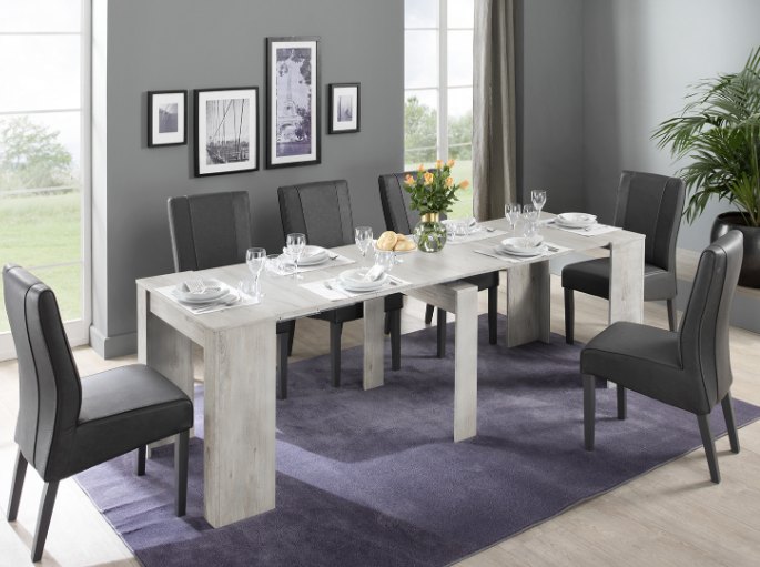 Longue table claire dépliée entourée de chaises noires dans un séjour