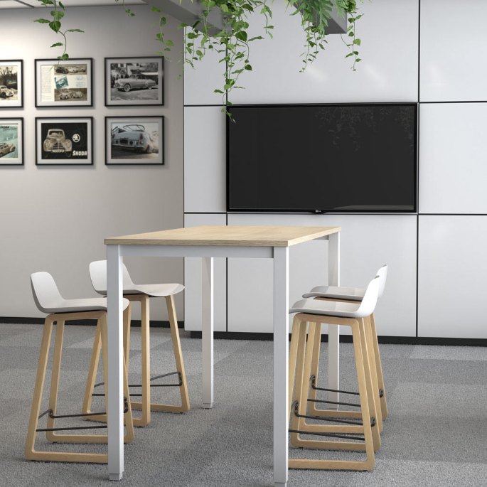 Plateau haut en bois clair et tabourets assortis face à un écran mural dans un bureau