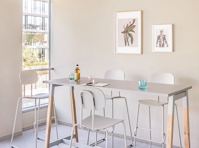 Plateau haut en bois clair à hauteur de comptoir, entouré de tabourets blancs