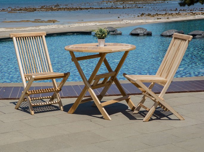 Petite table pliante à plateau rond entourée de deux assises en lattes claires sur une terrasse étroite