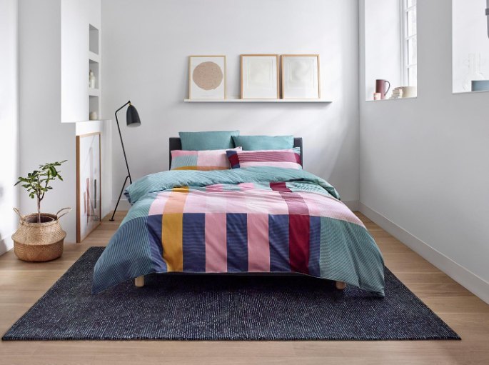 Lit double sur pieds posé sur un grand rectangle bleu nuit, au-dessus d'un parquet clair