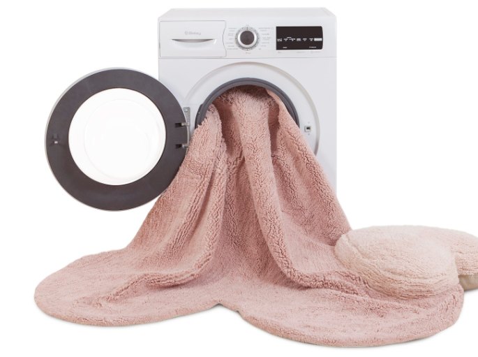 Petite carpette rose en coton sortant du hublot d'un lave-linge