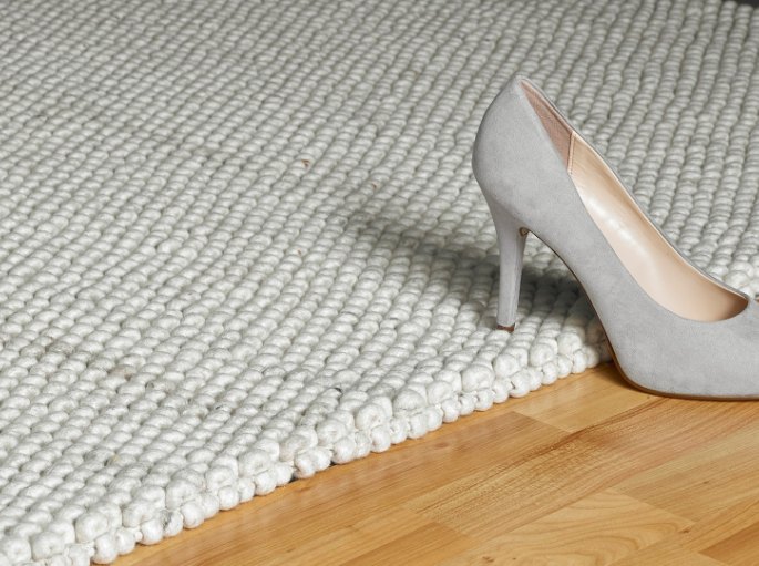 Escarpin gris posé sur un tissage clair, au bord d'un parquet en chêne