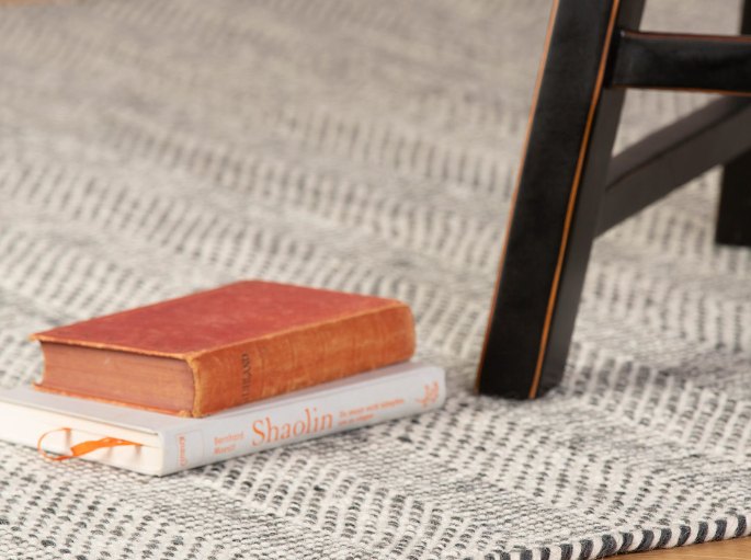 Pied de chaise noir et livres posés sur un tissage beige, sur un parquet